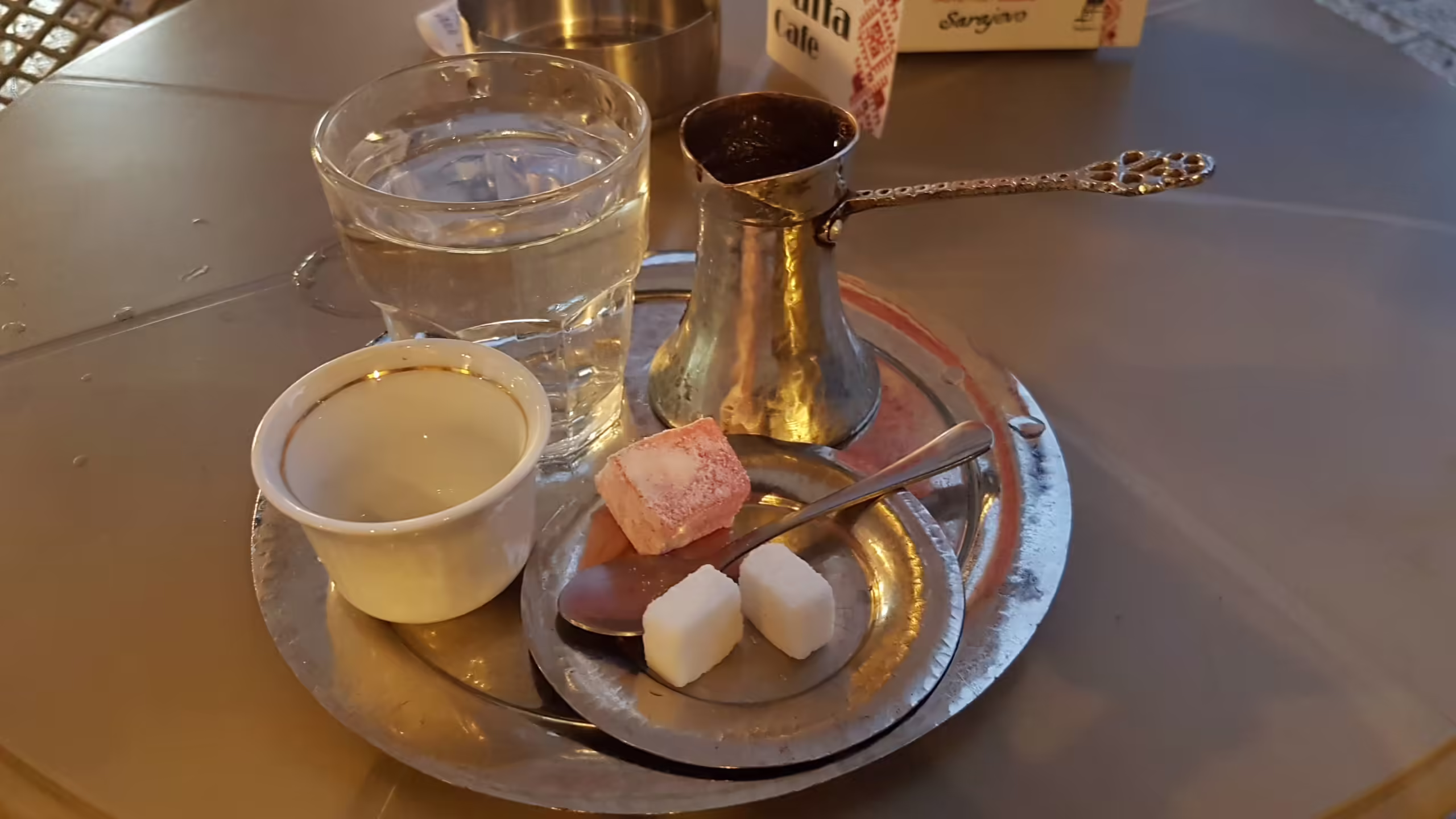 Bosnian coffee set with Turkish delight, sugar cubes, glass of water, spoon, cup, džezva and trays.