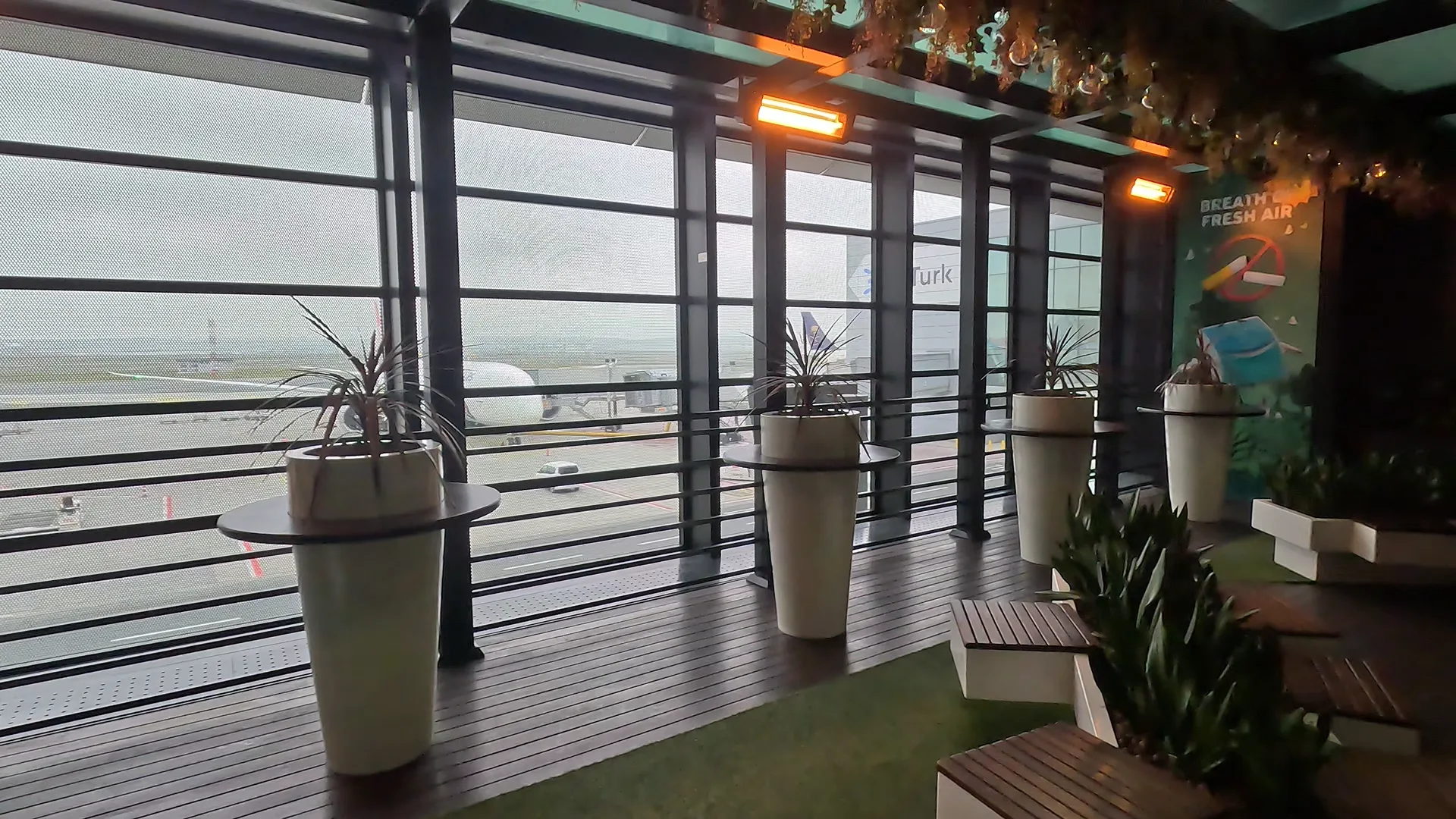 Istanbul Airport fresh air terrace with benches, plants, outdoor heaters and a view of planes.
