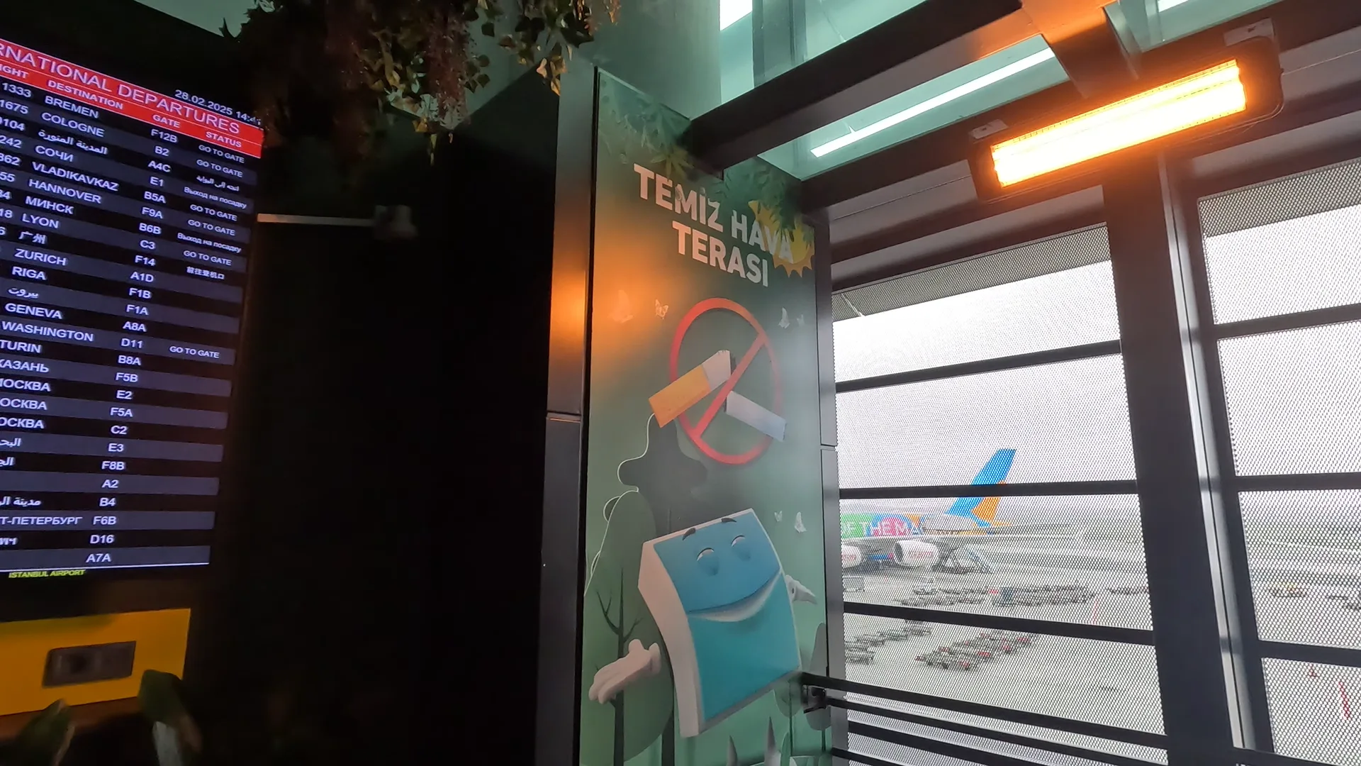 Istanbul Airport fresh air Terrace; outdoor heaters, plan timetable, no-smoking artwork and a view of the airport.