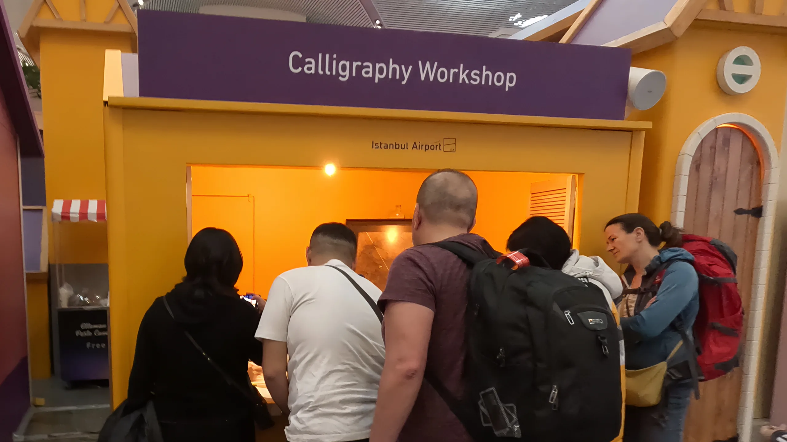 Crowd of people gathering around the Calligraphy Workshop stall at the Ramadan Village, Istanbul Airport.