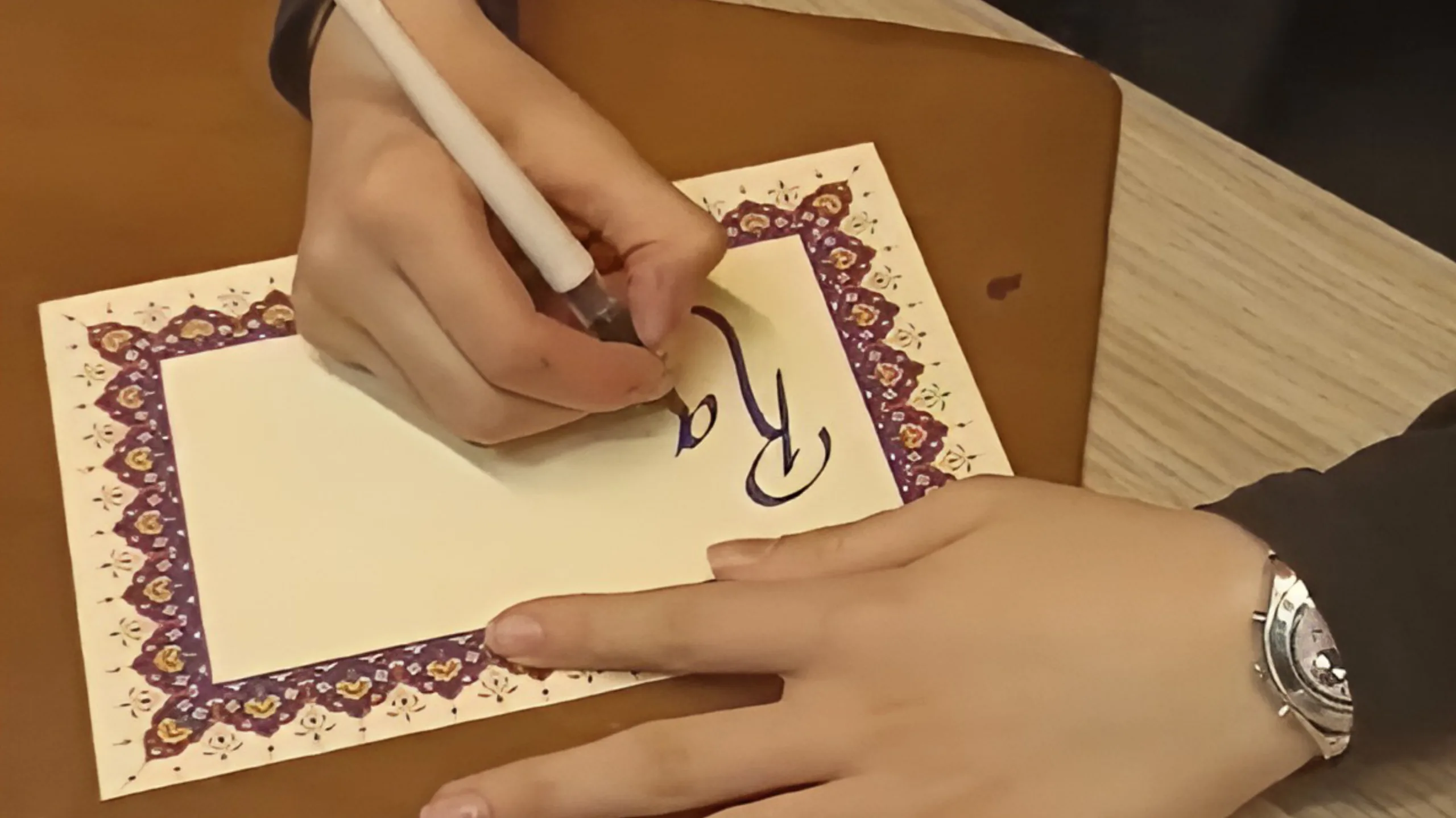 Calligrapher writing a custom message on a piece of paper with a patterned border.