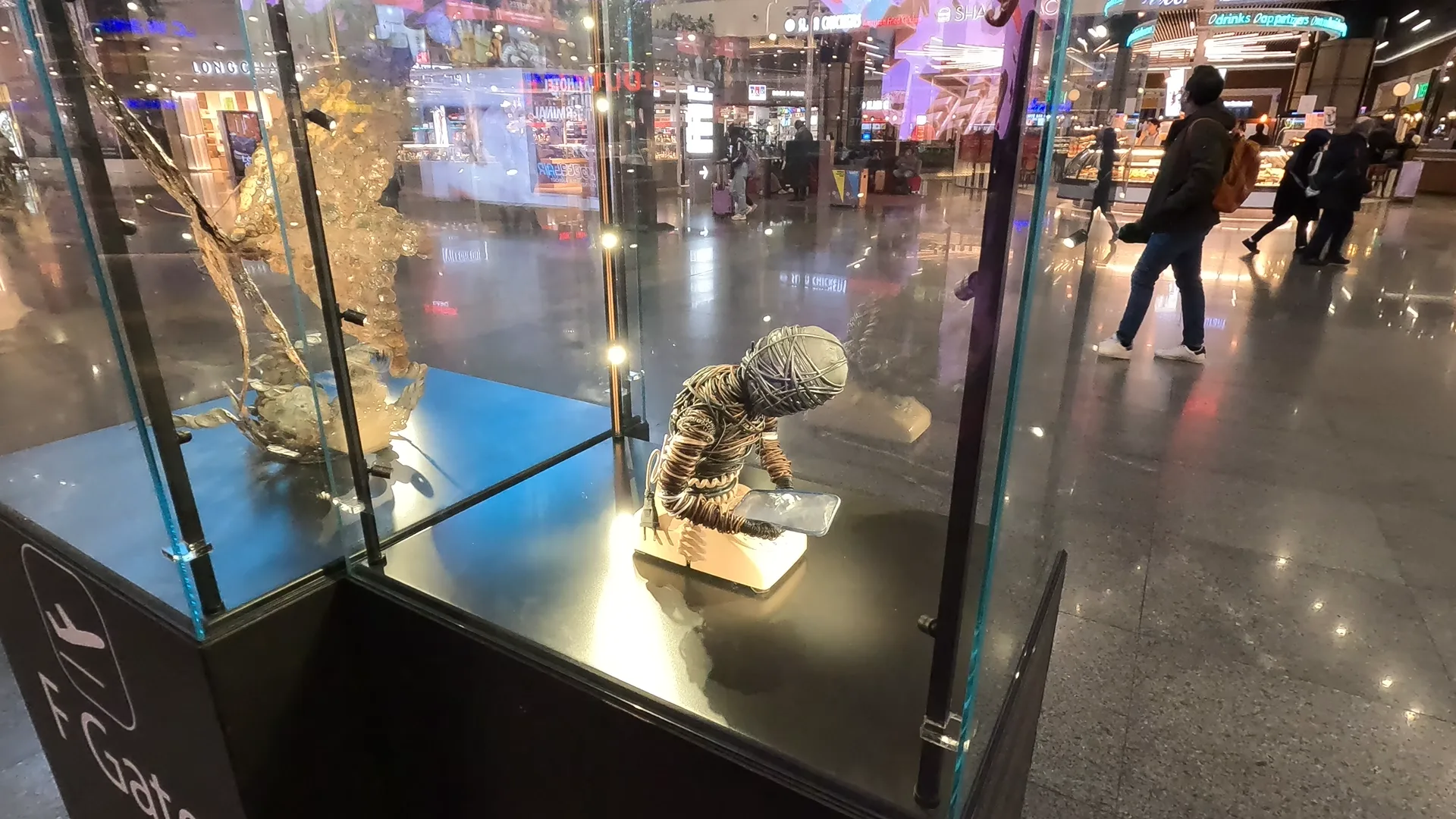 Artistic display in a glass panel of a man made of telephone wires hunched over, looking at his smartphone, at Istanbul Airport.